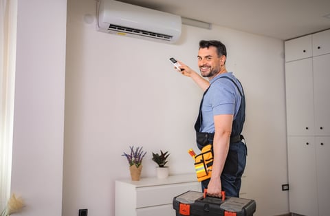 Technician installing a residential air conditioner and testing with remote control