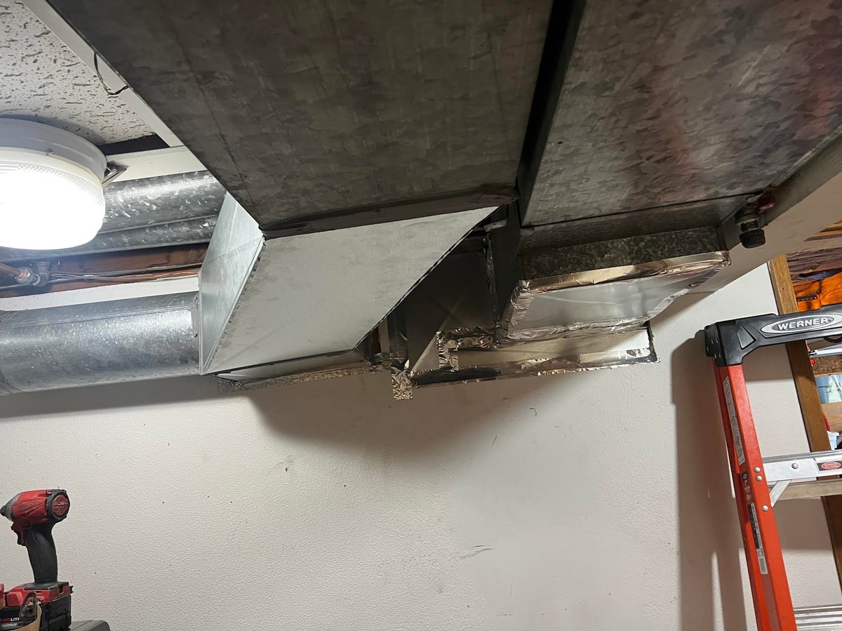 Overhead view of HVAC ductwork and metal piping in unfinished basement ceiling